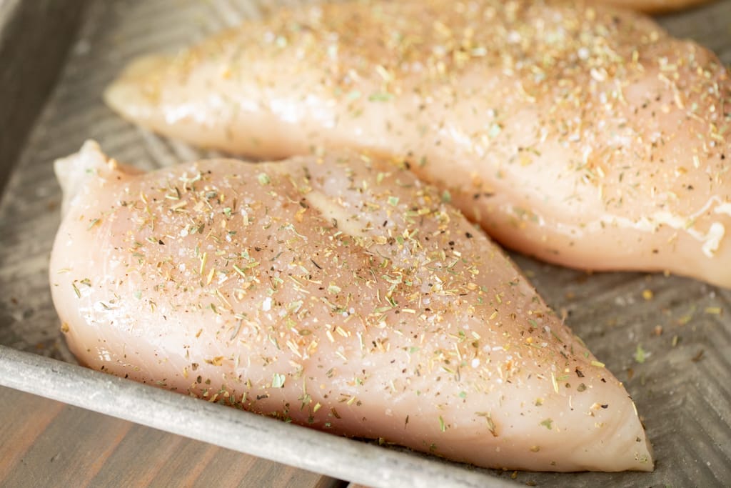 Raw, seasoned chicken breasts on a metal baking sheet.