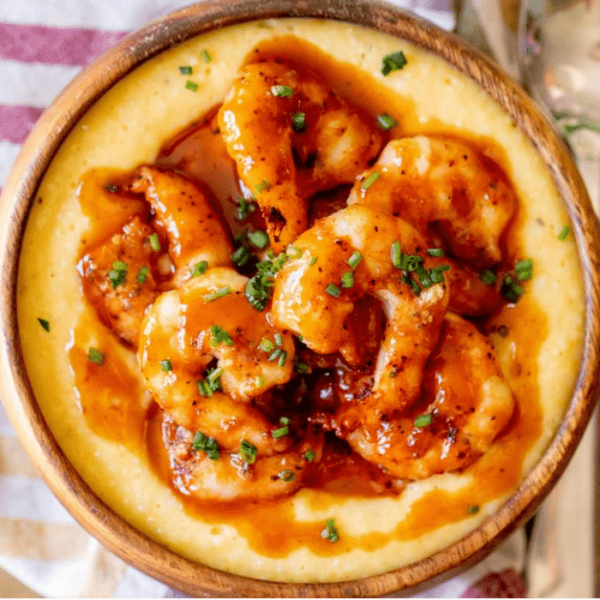 Overhead view of BBQ sauced shrimp on top of cheesy grits in a wooden bowl.