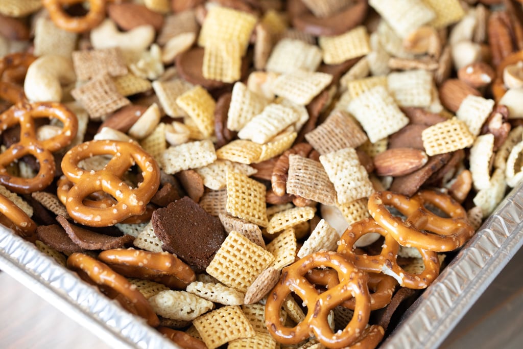 Chex cereal, mini pretzels, mixed nuts, and rye chips mixed in a disposable aluminum pan.