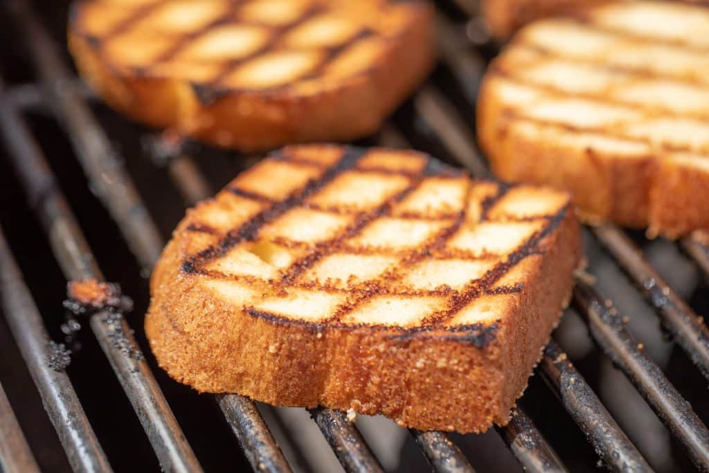 Thick slices of grilled pound cake on the grill grates of a grill.