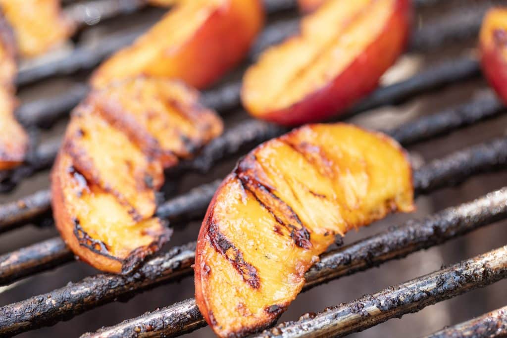 Sliced grilled peaches on the grill grates of a grill.