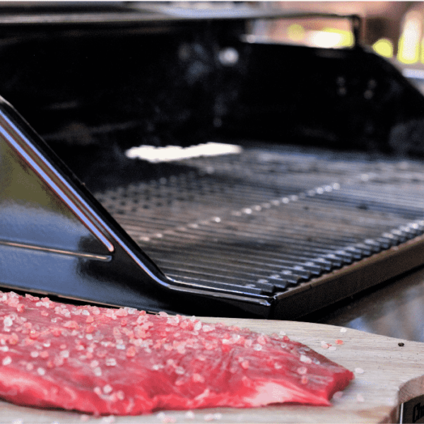Seasoned steak on a wooden board in front of an open grill.