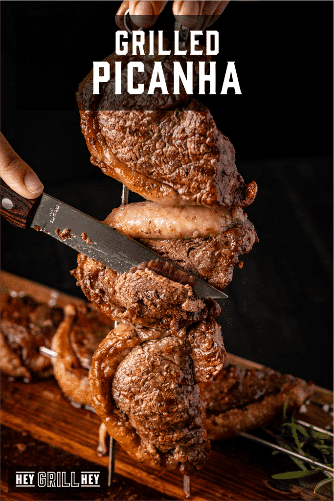 Knife slicing through picanha on metal skewers with text overlay - Grilled Picanha.