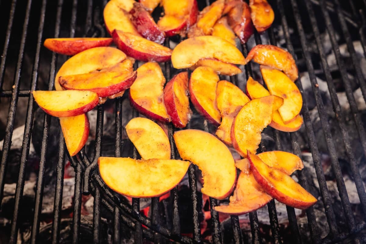 Peach slices on the grates of a grill.