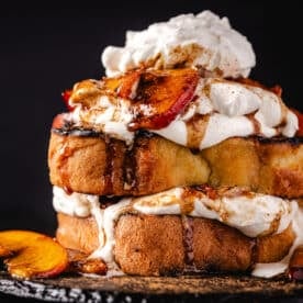 Pound cake slices topped with cream and peach slices on a black plate.