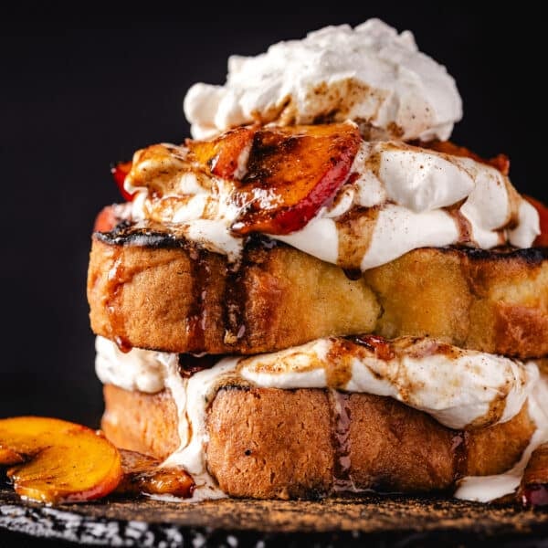 Pound cake slices topped with cream and peach slices on a black plate.