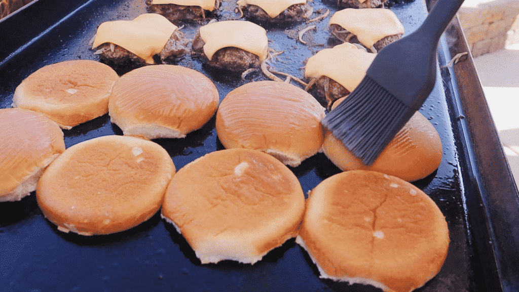 Burger buns and burger patties topped with American cheese on a flat top griddle.