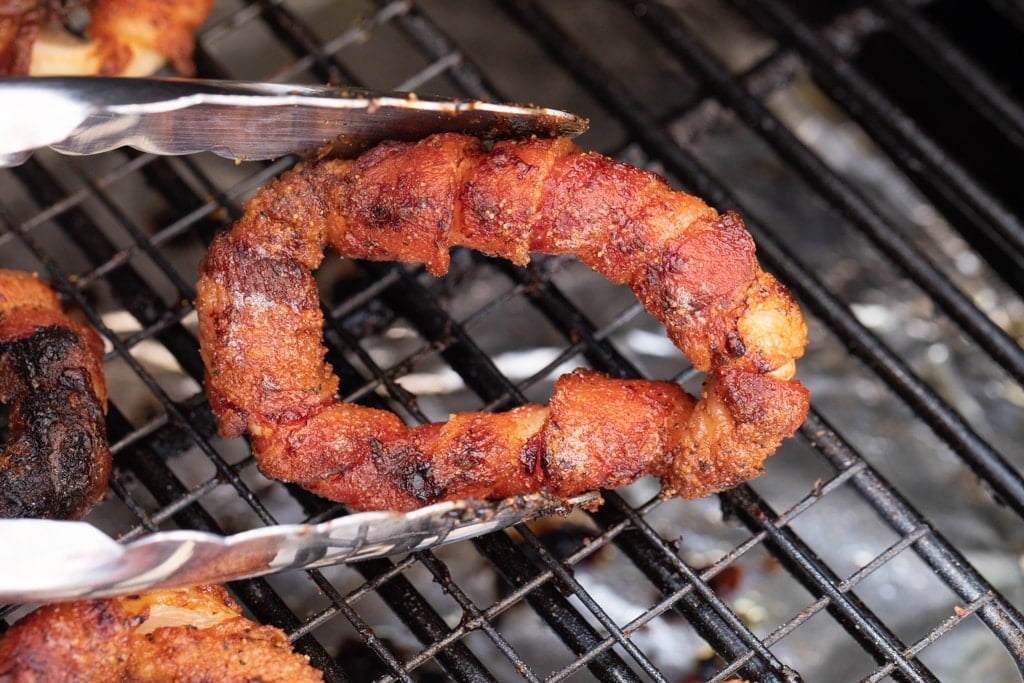 cooked bacon wrapped onion rings held with a pair of tongs