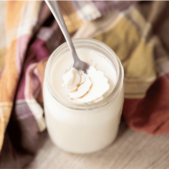 Spoon sticking out of a glass mason jar of chilled beef tallow next to a plaid towel.