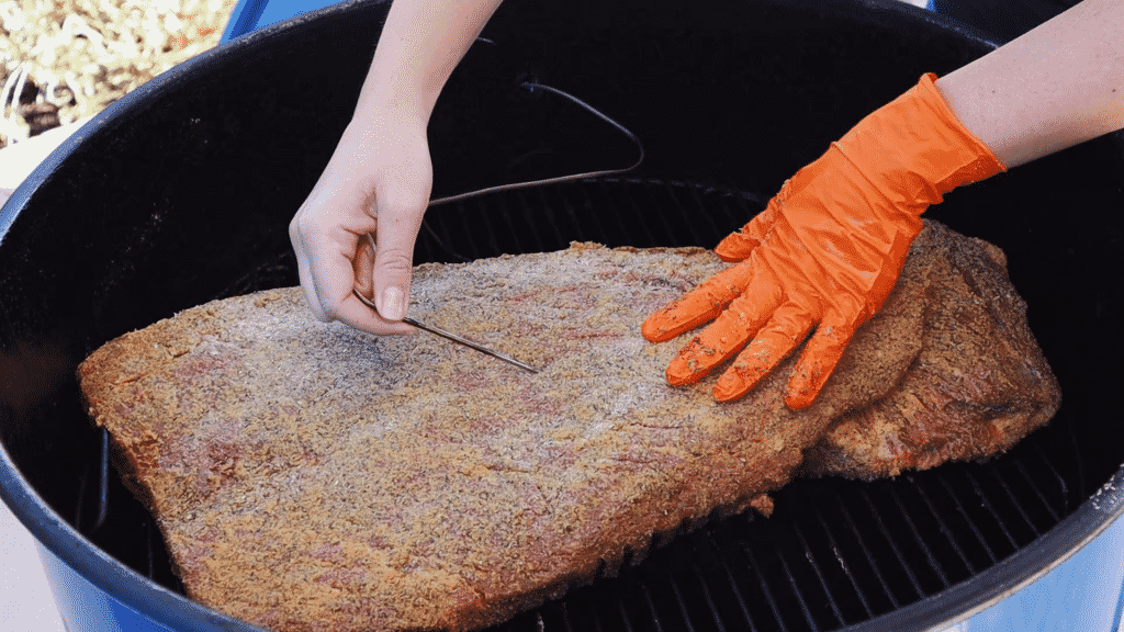 Inserting a temperature probe into a seasoned beef brisket.