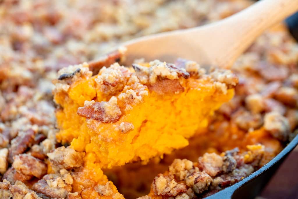 Wooden spoon taking a scoop out of a sweet potato casserole.
