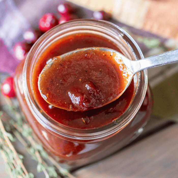 Spoonful of cranberry BBQ sauce resting on top of a glass mason jar of cranberry BBQ sauce.