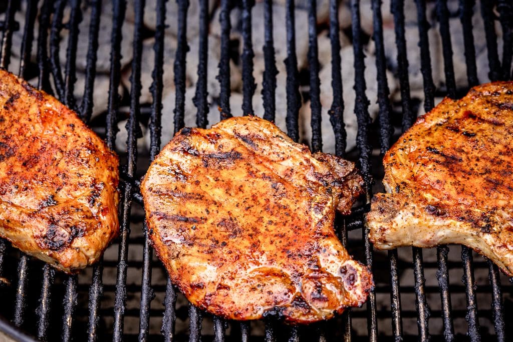 Three seasoned pork chops on the grill.