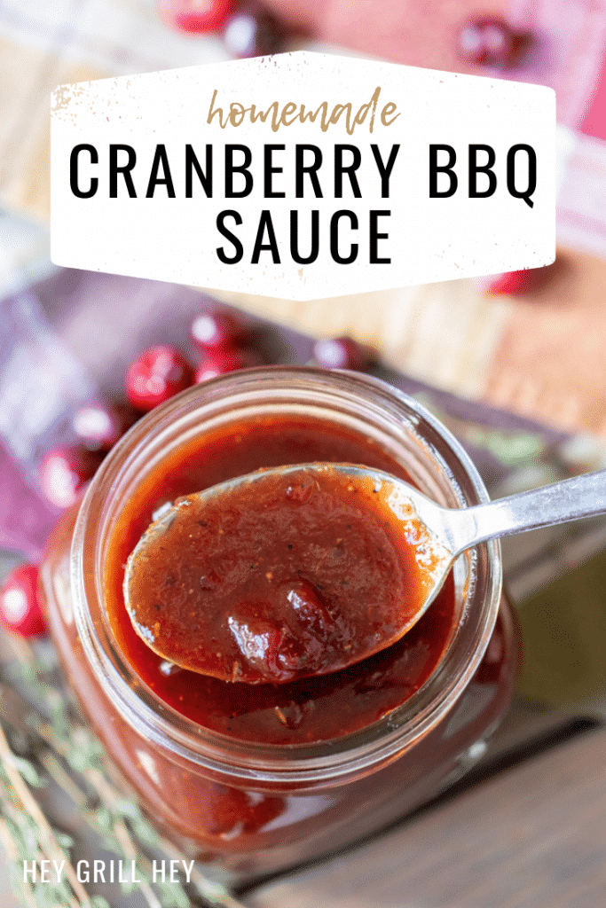 Spoonful of cranberry BBQ sauce resting on top of a glass mason jar of cranberry BBQ sauce. Text overlay reads: Homemade Cranberry BBQ Sauce.