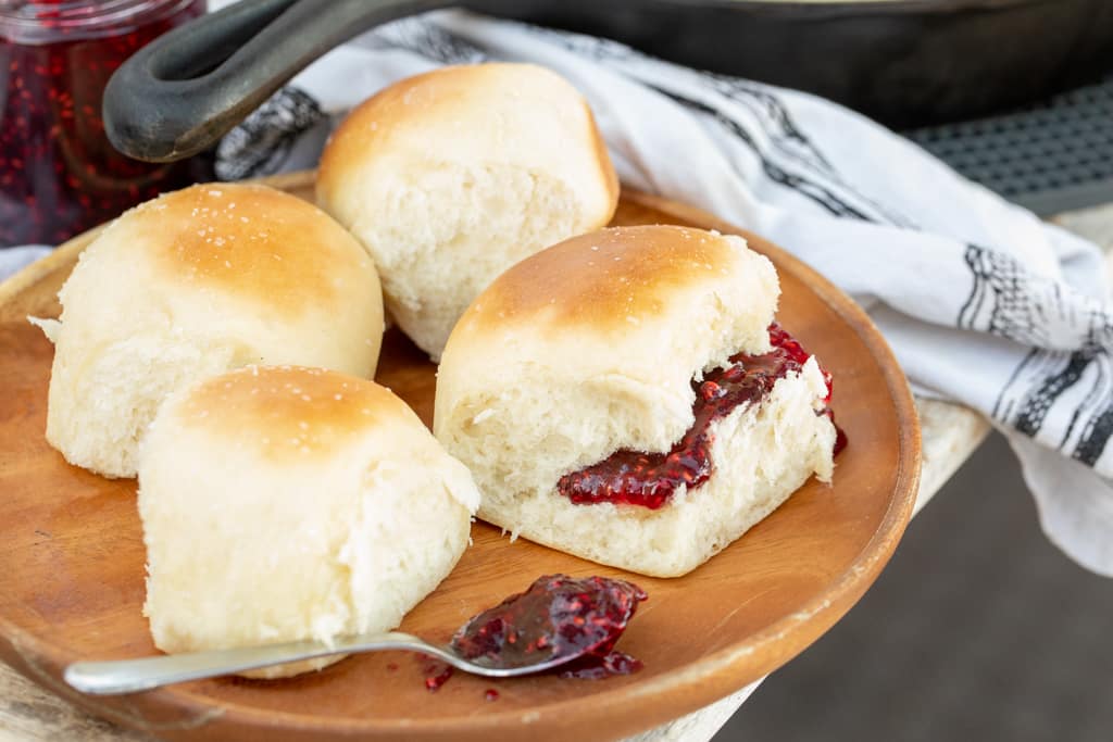 4 separated cooked rolls on a wooden plate and one roll has raspberry jam spread inside. 