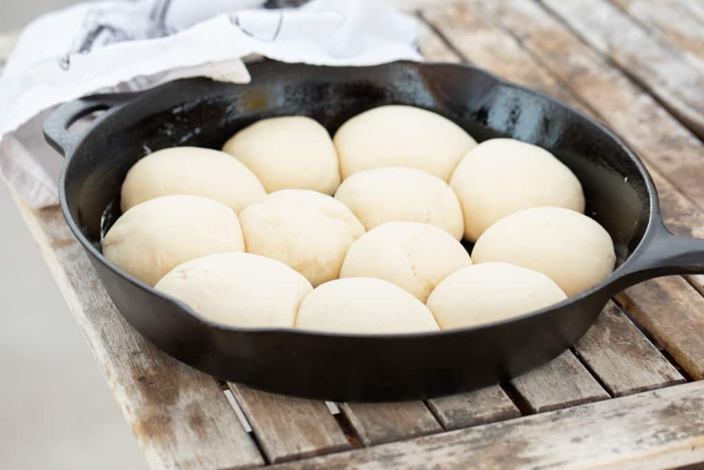 Twelve uncooked rolls in a cast iron skillet on a wooden table.