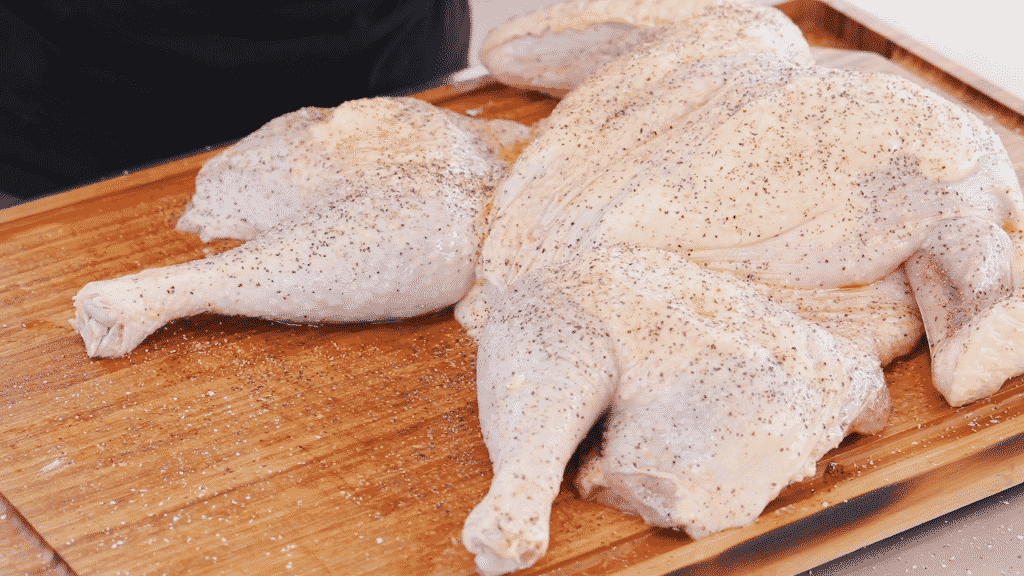 Uncooked, seasoned spatchcock turkey on a wooden cutting board.