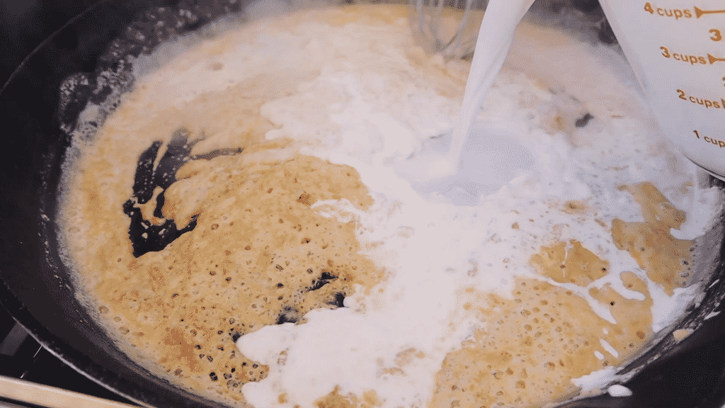 Half and half being poured into a roux in a cast iron skillet.