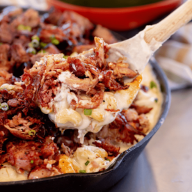 Smoked pulled pork mac and cheese being pulled out of a cast iron skillet with a wooden spoon.