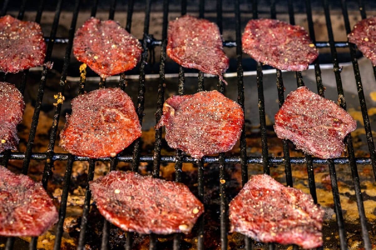 Jerky slices sitting on the grates of a smoker.