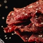 Jerky slices piled on a black serving platter, sprinkled with salt flakes.