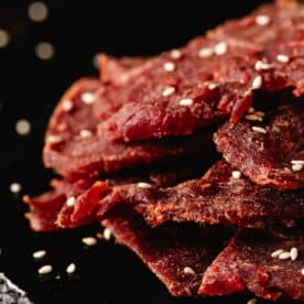 Jerky slices piled on a black serving platter, sprinkled with salt flakes.