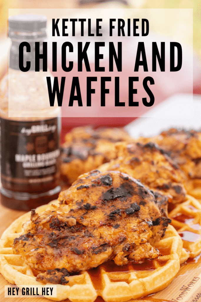 Four kettle fried chicken breasts on top of round waffles on a wooden cutting board with a bottle of BBQ sauce in the background. Text overlay reads: Kettle Fried Chicken and Waffles.