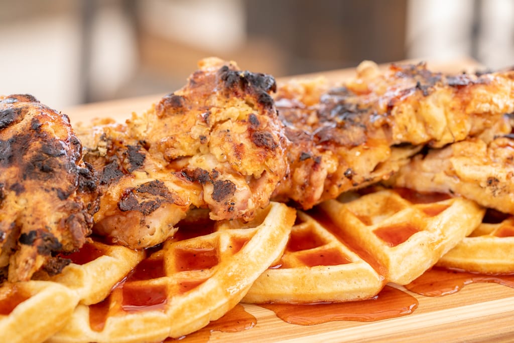 Grilled chicken breast on top of waffles on a wood cutting board glazed with sauce.