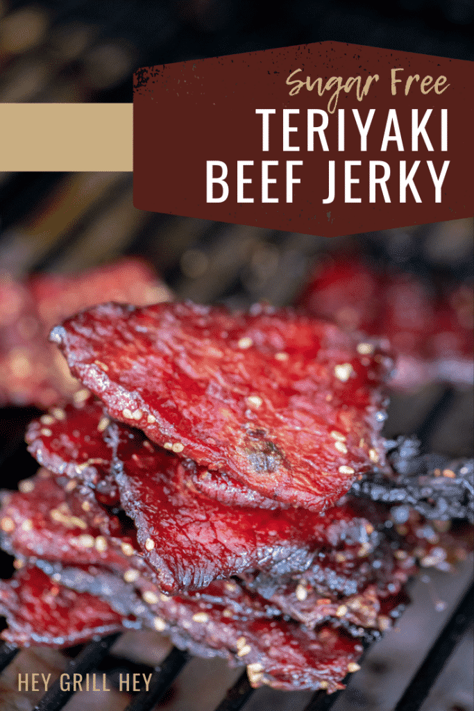Teriyaki sugar free beef jerky stacked on the grill grates of a smoker. Text overlay reads: Sugar Free Teriyaki Beef Jerky.