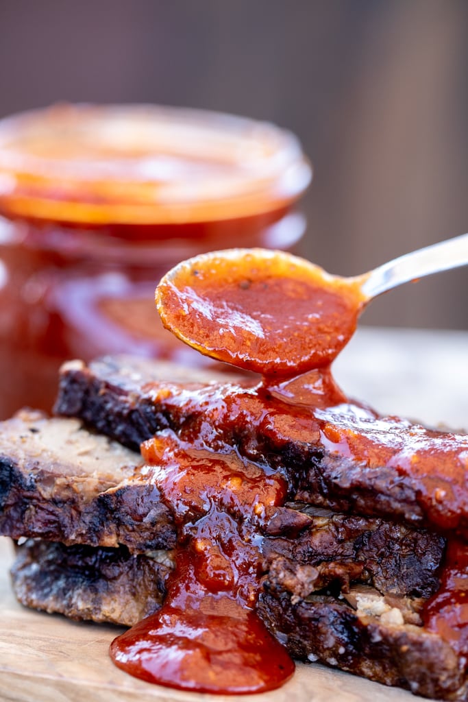 Texas BBQ Sauce being spooned over a stack of sliced brisket.