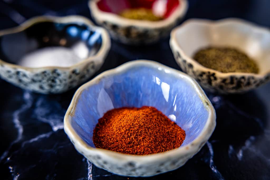 Four bowls full of ingredients for chili seasoning, including smoked paprika, salt, pepper, and seasonings.