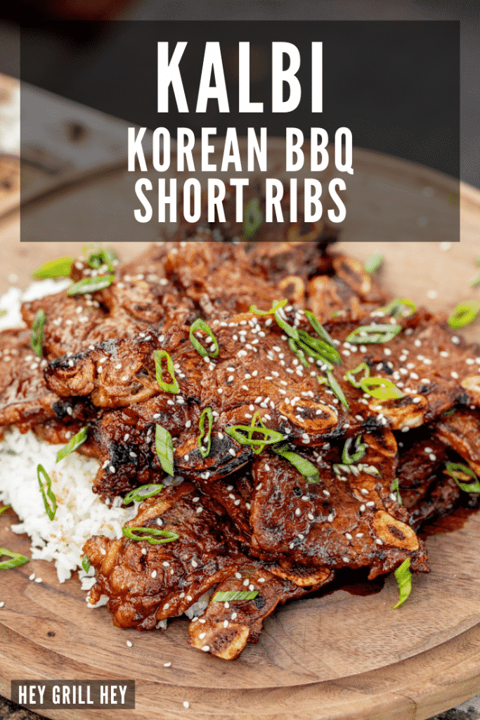 Kalbi garnished with sliced green onions and sesame seeds stacked on a round wooden serving board. Text overlay reads: kalbi Korean BBQ short ribs