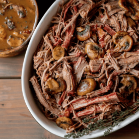 Guinness and mushroom braised and smoked shredded brisket in a white serving dish next to a small bowl of mushroom gravy.