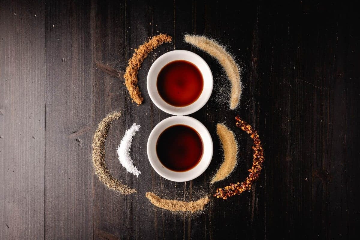 Worcestershire sauce and soy sauce in glass bowls, with lines of loose seasonings around them.