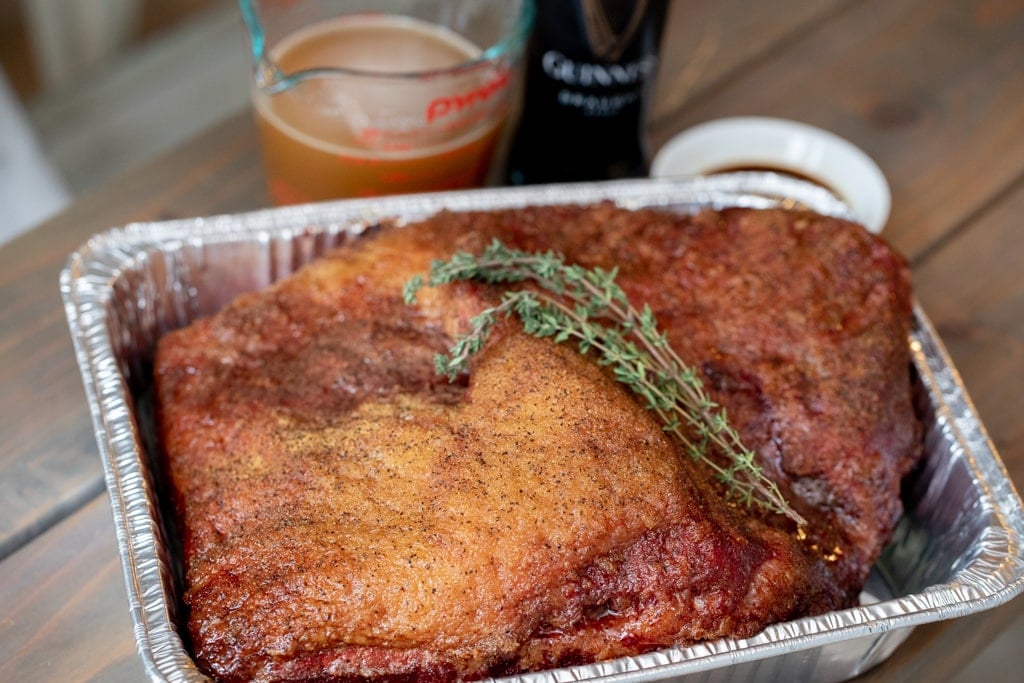 Seasoned brisket in a disposable aluminum pan garnished with rosemary sprigs.