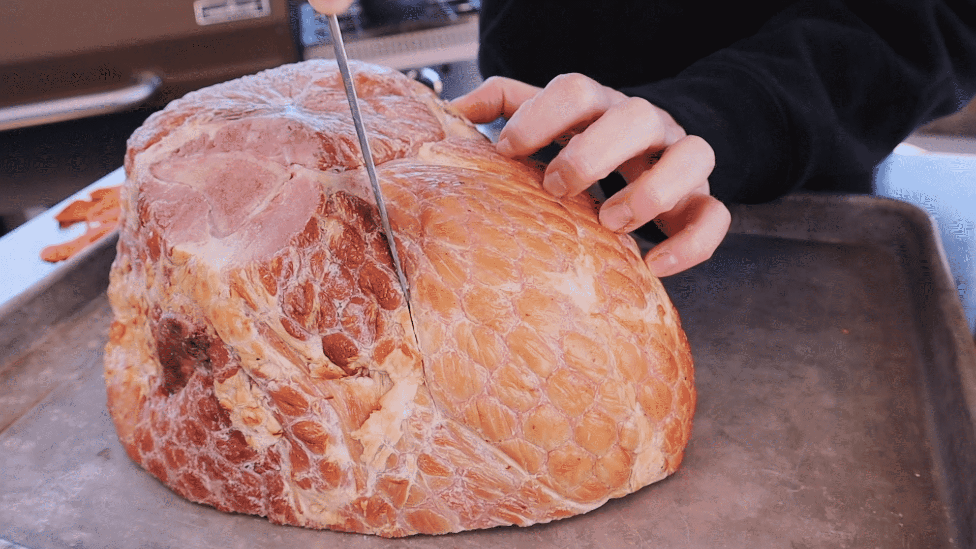 Susie uses a paring knife to make score marks across the surface of a whole picnic ham.