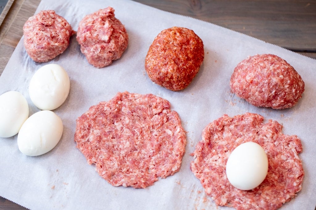 Breakfast sausage on parchment paper in various stages of being wrapped around eggs.