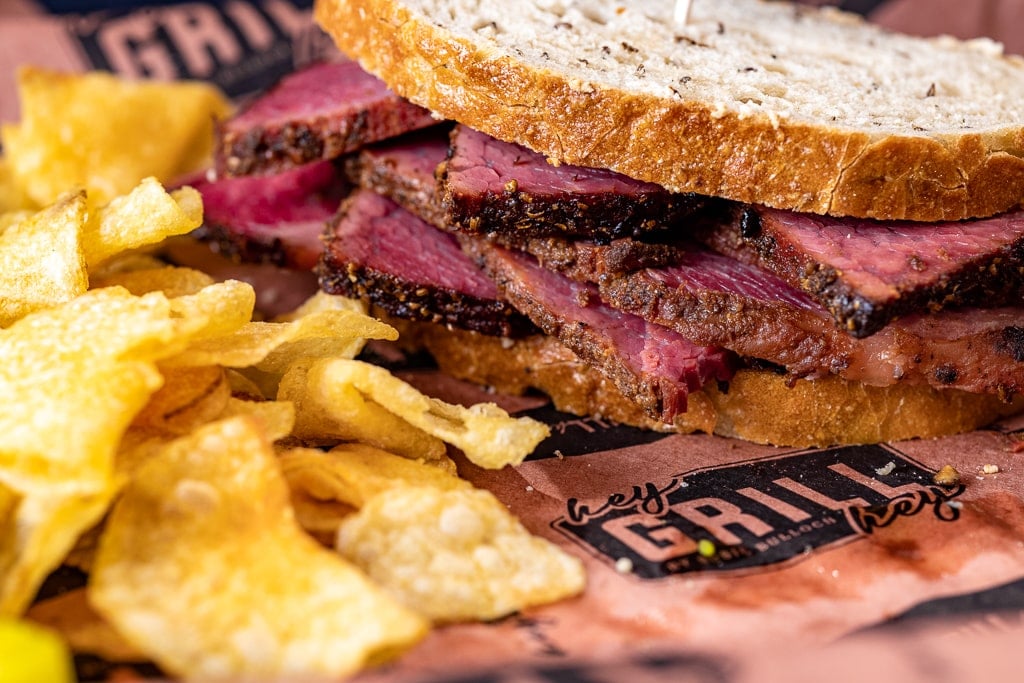 Pastrami sandwich on Hey Grill Hey butcher paper next to potato chips.