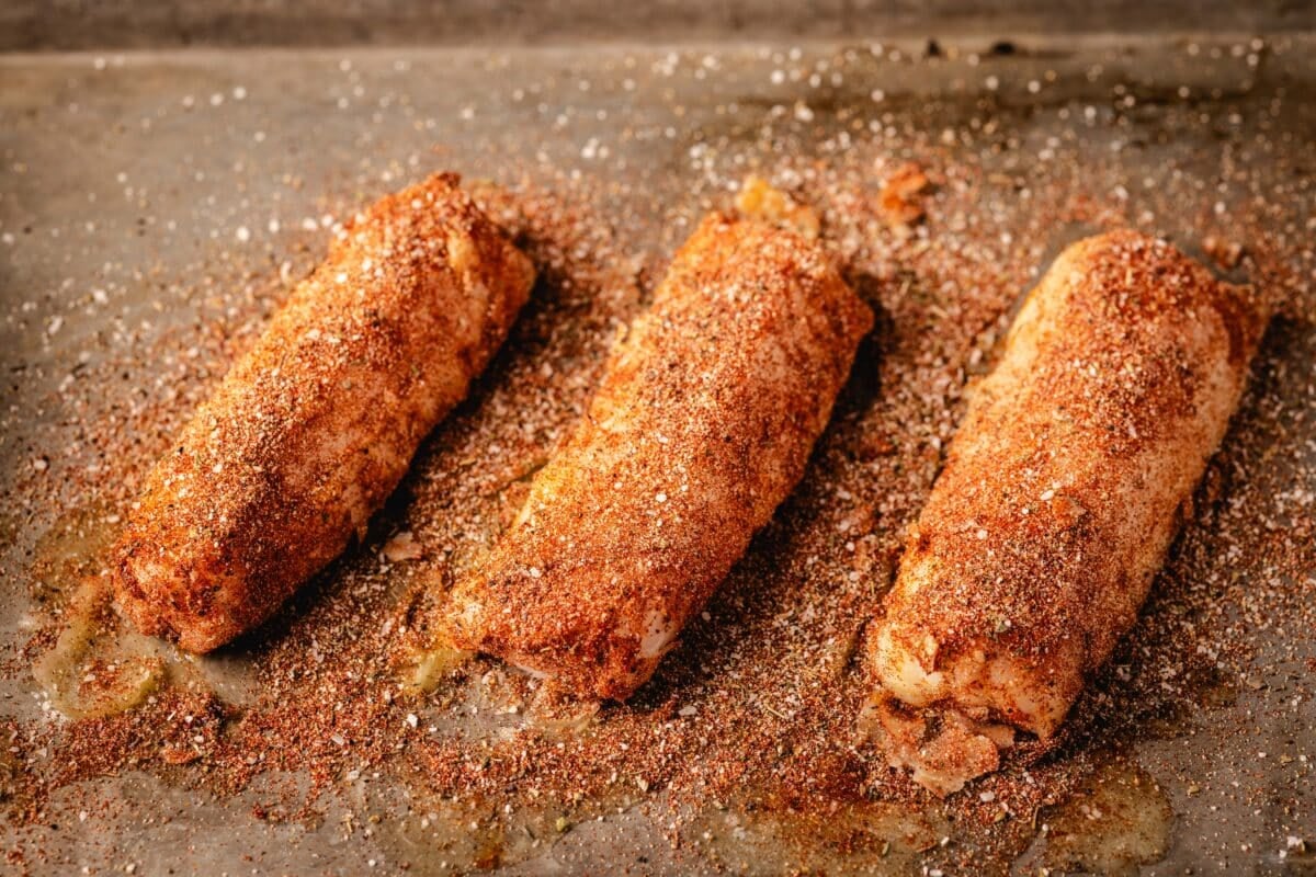 Three fish fillets on a baking sheet, all coated in blackened seasoning.