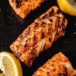 Grilled Mahi Mahi fillets and lemon wedges on a black surface.