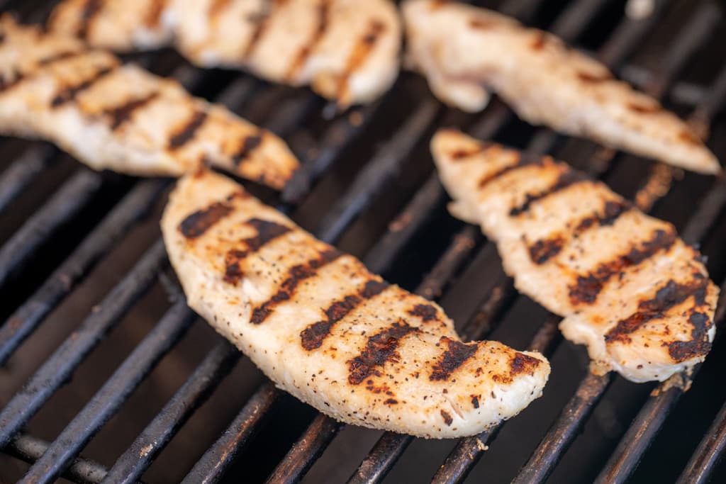 Seasoned chicken tenders on the grill grates of a grill.