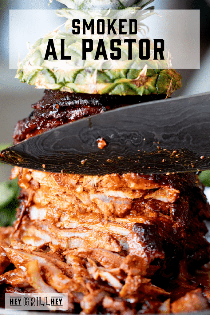 Chef's knife cutting into a stack of al pastor meat on a spit with text overlay - Smoked Al Pastor.