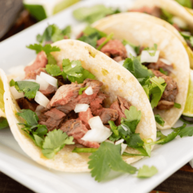 Two flank steak tacos topped with sliced onions and fresh cilantro on a white plate.
