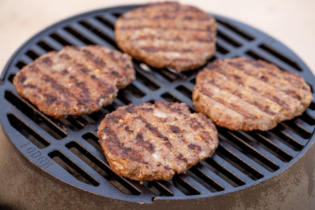 Four grilled bison burgers on the grill grates of a grill.