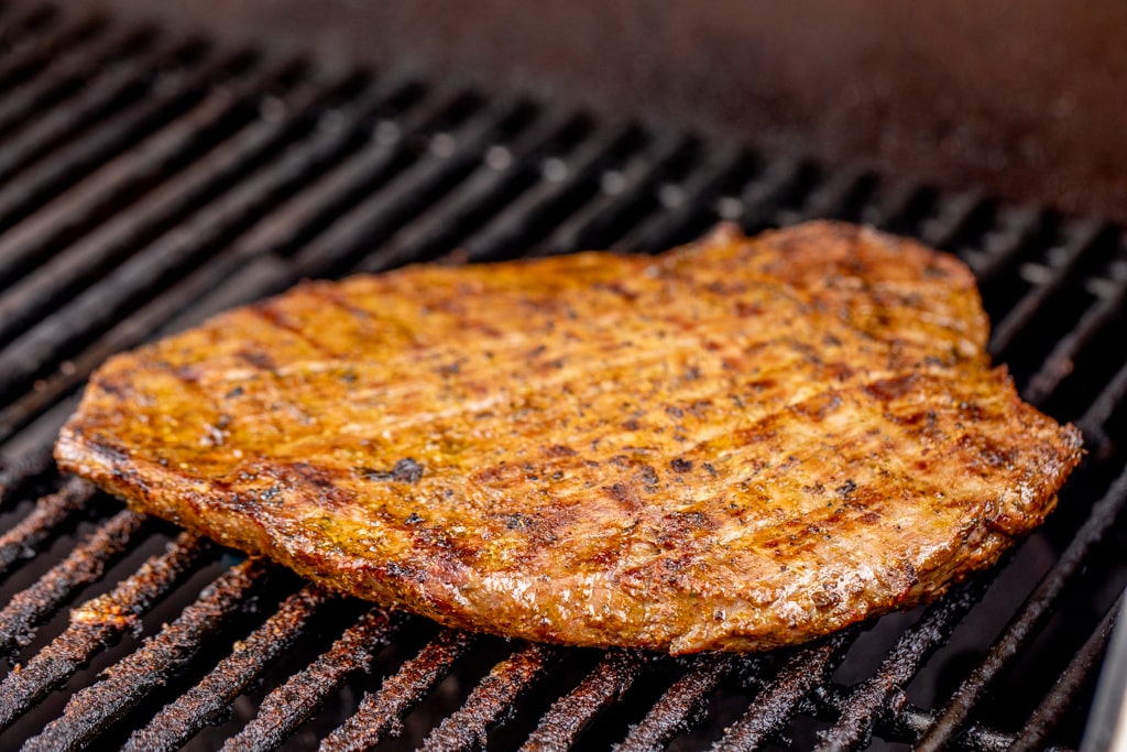Marinated flank steak on the grill grates of a gas grill.