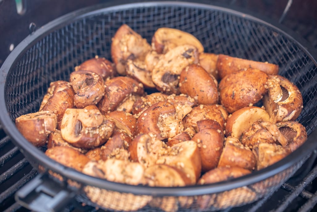 Grilled mushrooms in a grill basked on a gas grill.