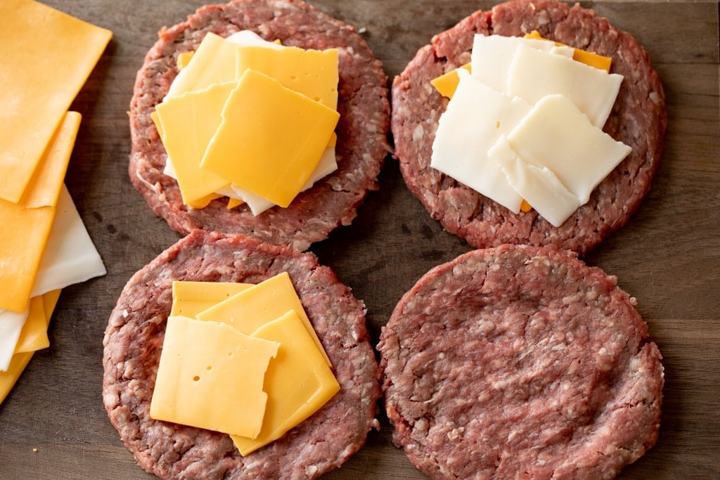 Formed burger patties covered with slices of cheese on a wood cutting board.