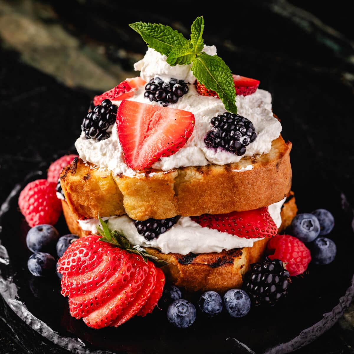 A pastry BBQ dessert topped with fresh cream, strawberries, blueberries, blackberries, and a mint garnish.