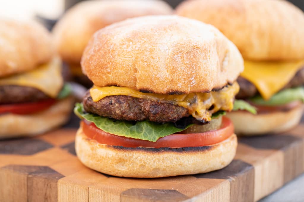 Grilled ranch bison burgers on a wooden cutting board.