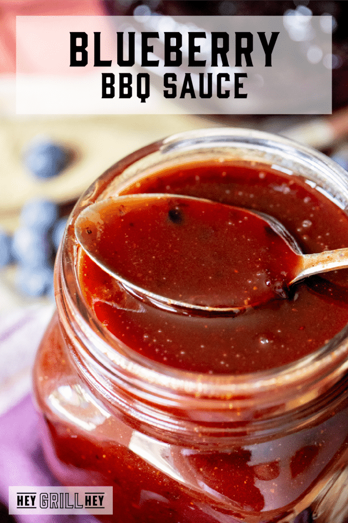 Blueberry BBQ sauce in a glass mason jar with a spoon resting on top of the jar with text overlay - Blueberry BBQ Sauce.